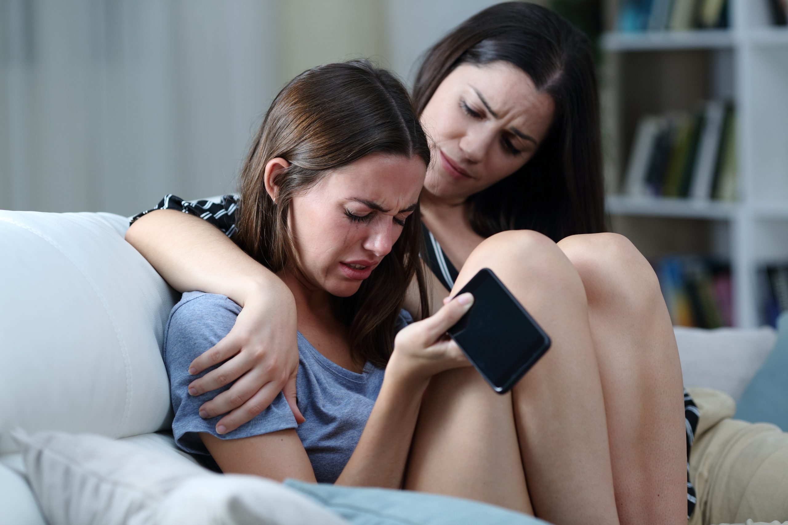 Sad teen with phone being comforted by her sister
